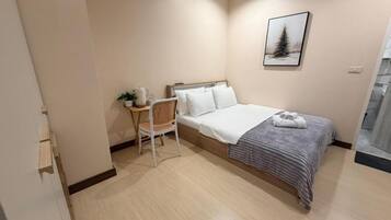 A bedroom with a bed, a chair, a bedside table, and a wall-mounted picture.