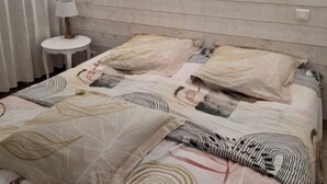 Quarto com cabeceira de madeira, duas camas com roupa de cama estampada, uma mesa redonda pequena com abajur e dois quadros pendurados na parede.