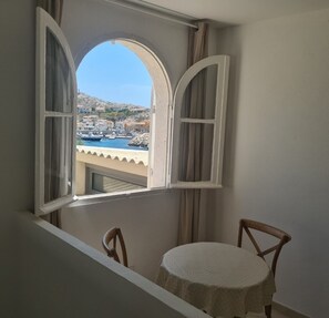 Ein Zimmer mit Blick auf eine Küstenstadt durch ein offenes Fenster mit weißen Fensterläden.