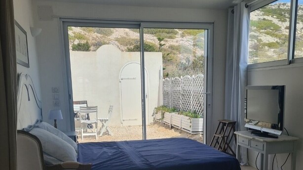 A bedroom with a bed, a desk with a computer, a chair, and a view of the outside.