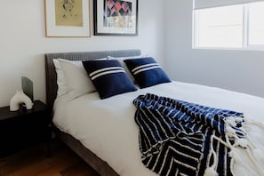 Een keurig opgemaakt bed met een gestreept dekbed, twee kussens en een nachtkastje met een vaas.