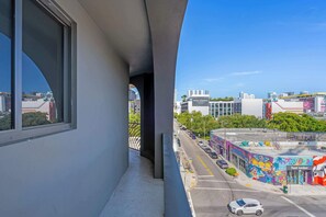 Ein Balkon mit Blick auf eine Stadtstraße, Gebäude und ein farbenfrohes Wandgemälde.