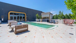 Zona junto a la piscina con sillas de descanso, una pileta pequeña y un edificio con acceso de vidrio.