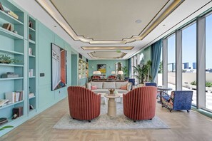 Eine moderne Hotelhalle mit einer Sitzecke, Bücherregalen und einem großen Fenster mit Blick auf die Stadt.