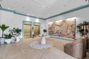 Un hall d’entrée avec une table ronde, deux ascenseurs, une grande peinture abstraite et des plantes en pot.