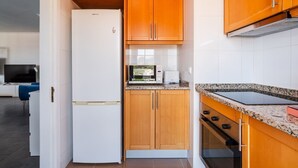 Eine kleine Küche mit einem weißen Kühlschrank, Holzschränken, einer Mikrowelle und einem Herd.