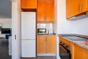 Eine kleine Küche mit einem weißen Kühlschrank, Holzschränken, einer Mikrowelle und einem Herd.