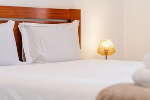 Ein ordentlich bezogenes Bett mit weißen Leinen und Kissen, ein Holzkopfbrett und eine Nachttischlampe.