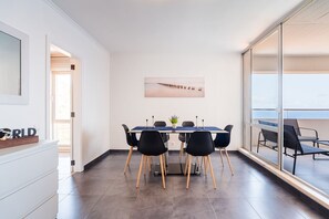A modern dining area with a table, chairs, and a view of the sea through large windows. - GuestReady - Oceanview Retreat in Caniço (Caniço de Baixo)