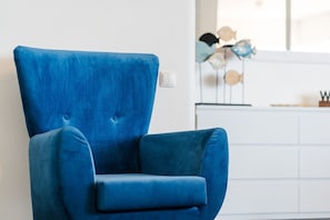 Ein blauer Sessel mit hoher Rückenlehne und gepolstertem Sitz, vor einer weißen Wand platziert.