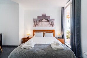 A hotel room with a bed, two bedside lamps, a window with curtains, and a wall-mounted artwork. - GuestReady - Oceanview Retreat in Caniço (Caniço de Baixo)