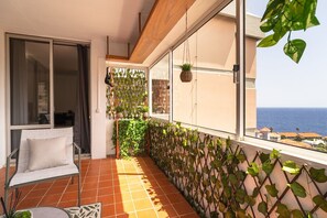 Un balcon avec une chaise, des plantes en pot et une vue sur la mer.