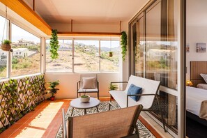 A balcony with a view of a hilly landscape, a seating area with a table, and a bed. - GuestReady - Oceanview Retreat in Caniço (Caniço de Baixo)