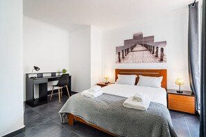 A hotel room with a bed, a desk, a chair, a nightstand, and a wall-mounted artwork. - GuestReady - Oceanview Retreat in Caniço (Caniço de Baixo)