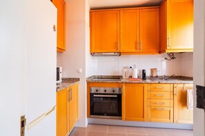 A kitchen with wooden cabinets, a built-in oven, and a granite countertop. - GuestReady - Oceanview Retreat in Caniço (Caniço de Baixo)