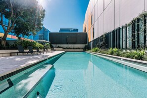 Ein Schwimmbecken mit Liegestühlen und einem modernen Gebäude im Hintergrund.