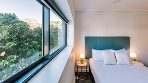 A hotel room with a bed, bedside lamps, a window with a view of trees, and a ceiling fan. - Two Bedroom Sanctuary in the Valley (Fortitude Valley)