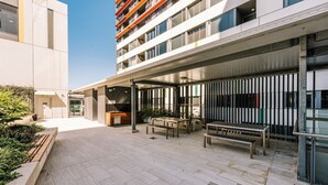 A modern outdoor area with a covered seating area, a reception desk, and a building with multiple floors and balconies. - Two Bedroom Sanctuary in the Valley (Fortitude Valley)