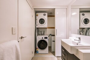 Ein kleines Hotelbad mit Waschmaschine, Trockner und Waschbecken inklusive Spiegel.