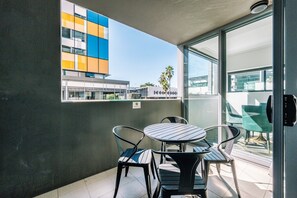 A balcony with a table and chairs, a view of a modern building, and a door to the right. - Two Bedroom Sanctuary in the Valley (Fortitude Valley)