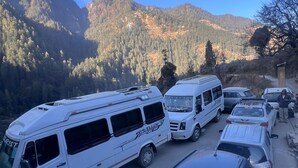 A parking area with several white RVs and cars, surrounded by mountains and trees.