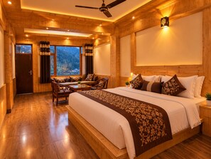 A hotel room with a large bed, a seating area with chairs, a ceiling fan, and a view of the outdoors. - Sunshine By Nature Crest  (Jibhi)