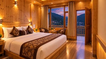 Un dormitorio con piso de madera, una cama grande, una mesita de noche, una silla y vistas a un paisaje montañoso a través de un ventanal.