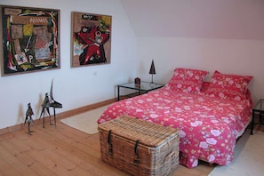 A bedroom with a large bed, two posters on the wall, a small table, and a wicker basket. - Luxurious Villa in Locquirec with Terrace (Locquirec)