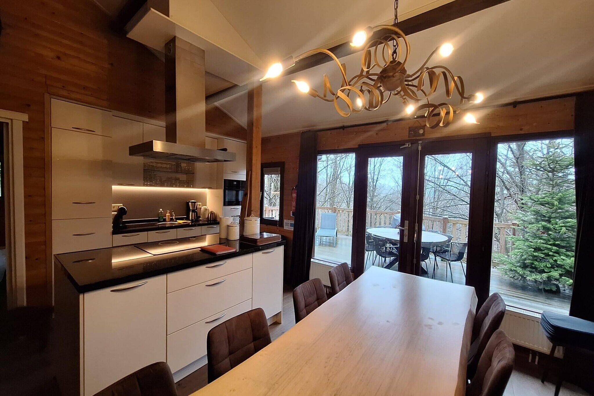 A modern kitchen with a dining area, wooden walls, and a large window overlooking a deck.