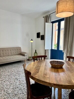 A dining area with a round wooden table, chairs, a bowl, a floor lamp, and a sofa. - Casa Fioraliso, a cozy retreat in the heart of Noto's historic center. (Noto)