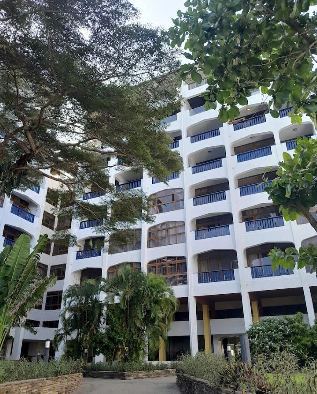 A multi-story building with balconies, surrounded by greenery and trees.