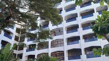 A multi-story building with balconies, surrounded by greenery and trees.