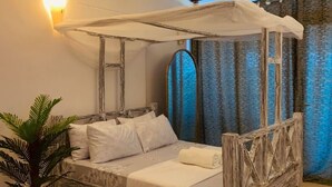 A bed with a canopy, a potted plant, and a wall-mounted light fixture. - Samara Studio Beachfront Apartment - Diani Beach (Diani Beach)