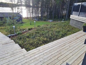 Une terrasse en bois, avec une zone herbeuse et une étendue d’eau en arrière-plan.