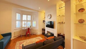 Ein Wohnzimmer mit einer Couch, einem Fernseher, einem Kamin und einem Fenster mit Jalousien.