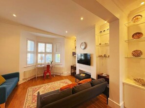 A living room with a sofa, a television, a fireplace, and a window with blinds. - Large family house 5 mins walk from station free parking (London)