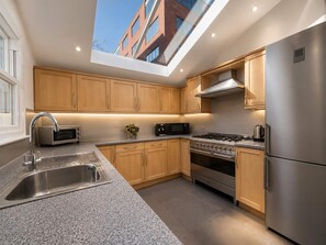 A modern kitchen with a skylight, stainless steel appliances, and wooden cabinetry. - Large family house 5 mins walk from station free parking (London)