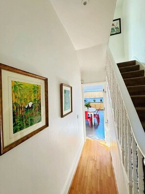 A hallway with a staircase, wooden flooring, and framed artwork on the walls. - Large family house 5 mins walk from station free parking (London)