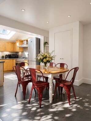 A modern kitchen with wooden cabinets, a stainless steel refrigerator, and a dining area with a wooden table and red chairs. - Large family house 5 mins walk from station free parking (London)