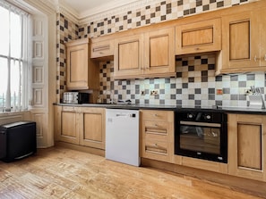 A kitchen with wooden cabinets, a dishwasher, an oven, and a checkered backsplash. - A Georgian apartment in Mariner’s House, beside Little Pannett Park in Whitby. (Whitby)