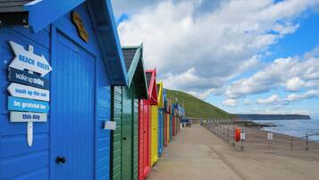 A row of colorful beach huts with directional signs and a coastal view.