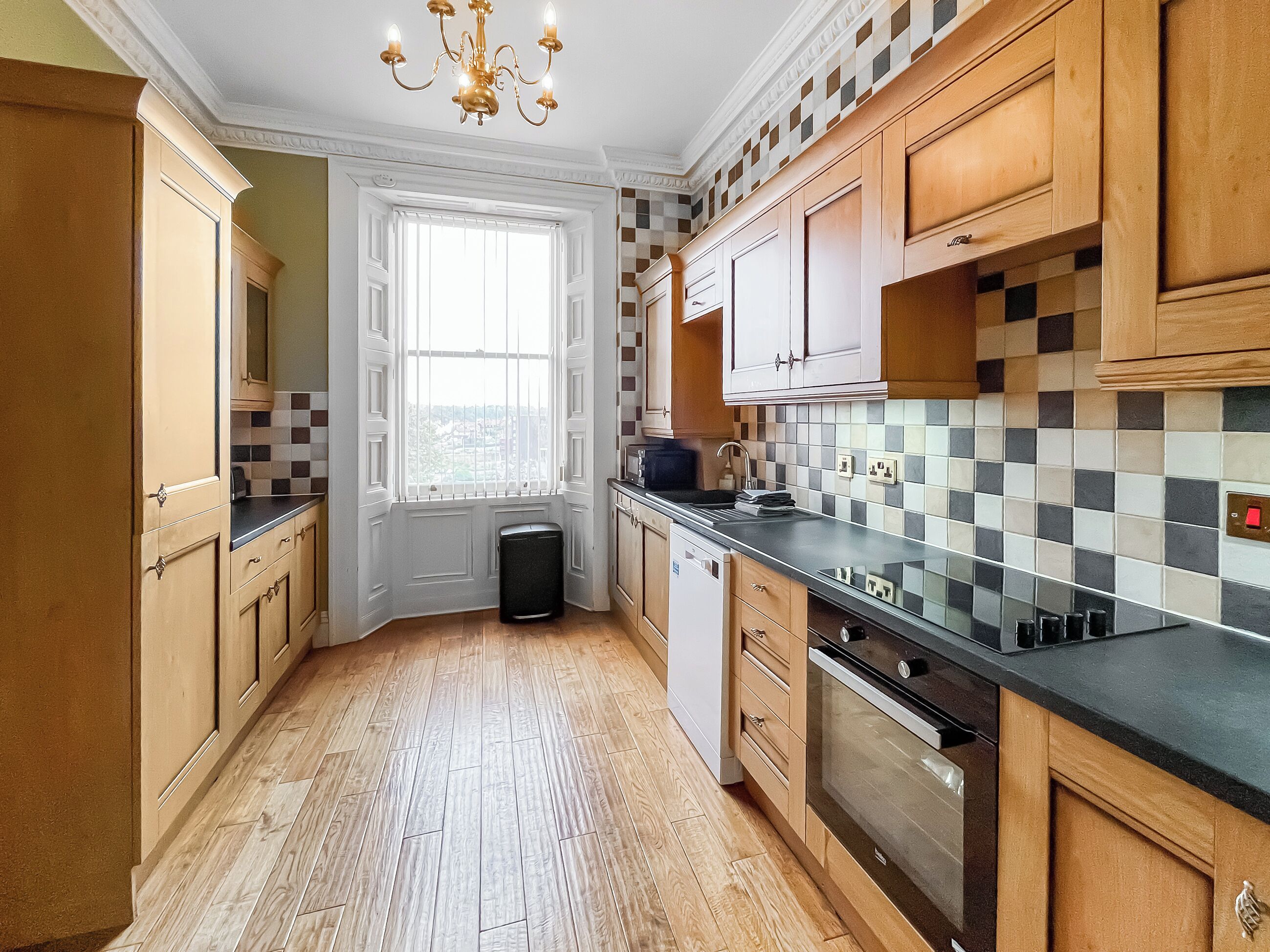 A kitchen with wooden cabinets, a black countertop, a built-in oven, and a window with a view.