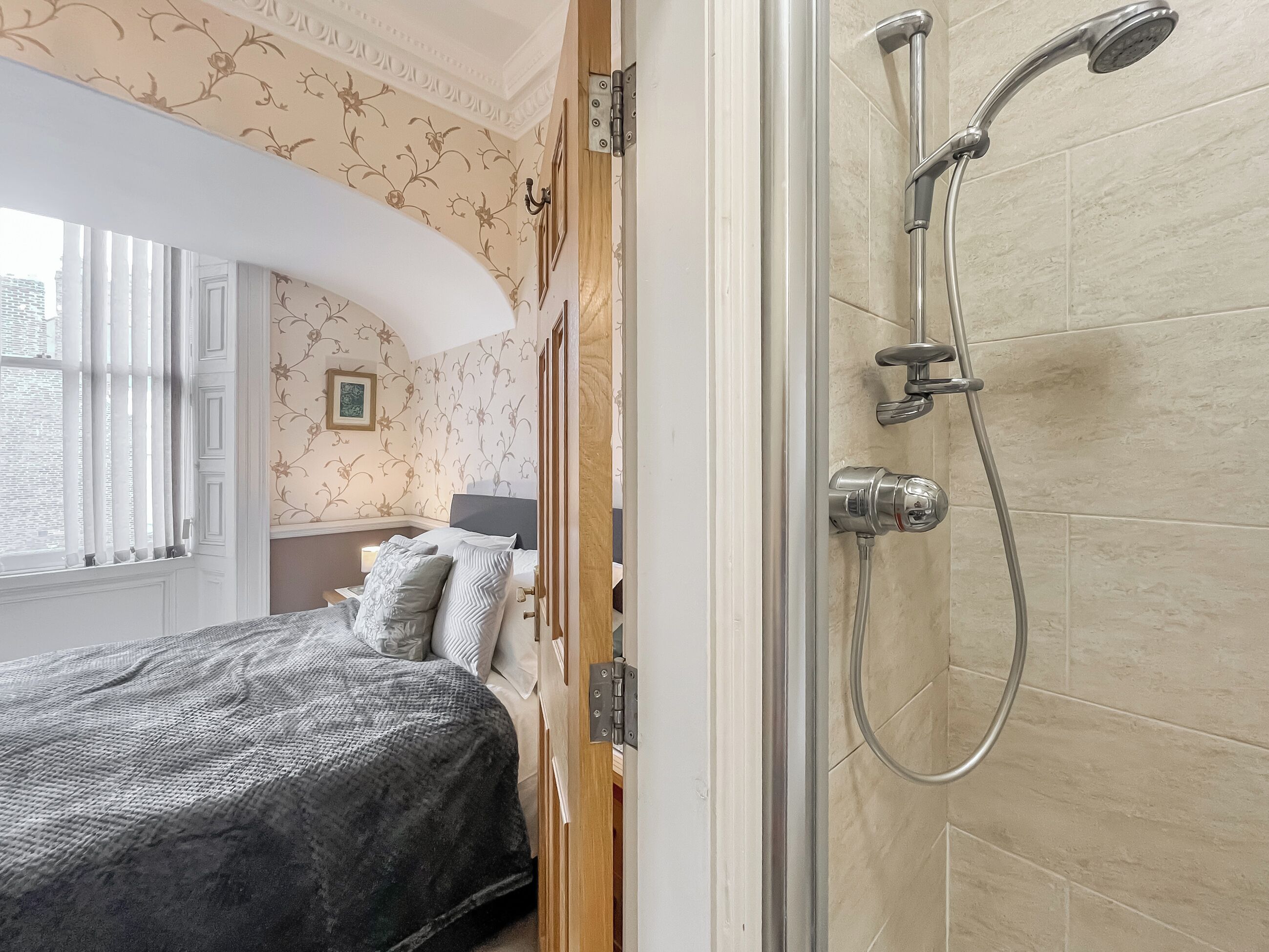 A hotel room with a bed, a shower, and a window with curtains.