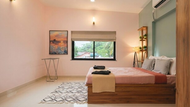 Um quarto com cama, janela com vista, mesa de cabeceira e prateleira na parede com plantas.