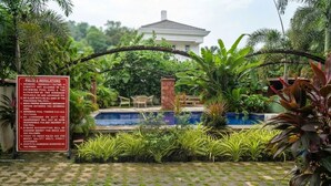 Uma piscina rodeada por vegetação exuberante e um edifício branco ao fundo.
