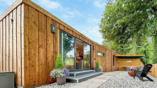 Een modern houten gebouw met een glazen deuropening, terrasplekken en een patio met grind.