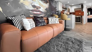 Een moderne woonkamer met een bruine leren bank, een groot abstract schilderij en decoratieve kussens.