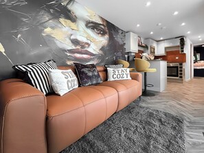 A modern living room with a brown leather sofa, a large abstract painting, and decorative pillows. - 1 bedroom accommodation in Stranraer (Stranraer)