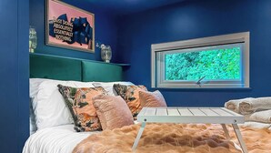 Een slaapkamer met een bed, kussens, een raam met uitzicht en een muur met een poster.