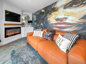 A living room with a fireplace, a large abstract painting, and a sofa with decorative pillows. - 1 bedroom accommodation in Stranraer (Stranraer)